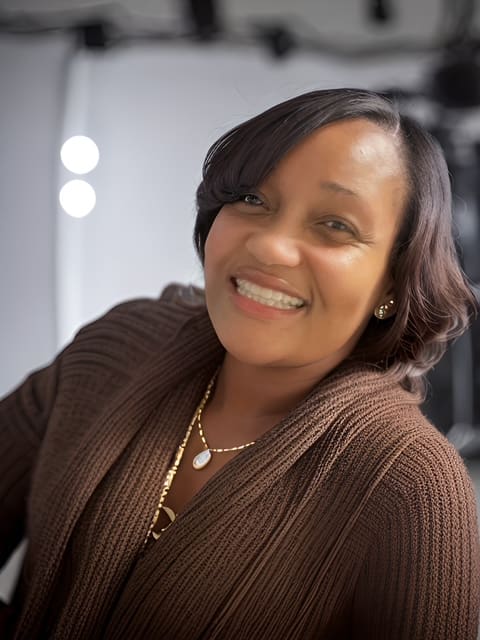 A woman smiling for the camera in a brown sweater.