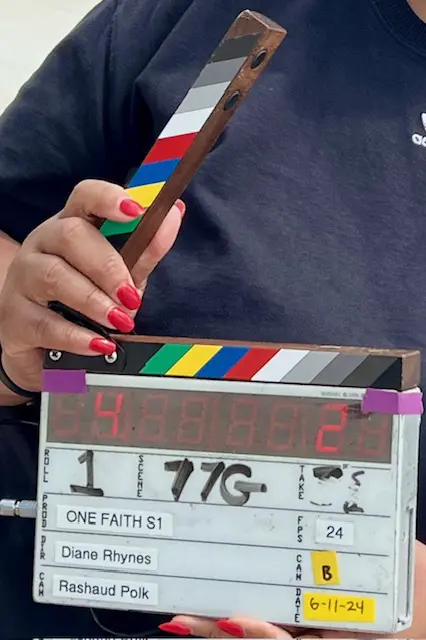 A person holding a clapperboard in front of a movie slate.